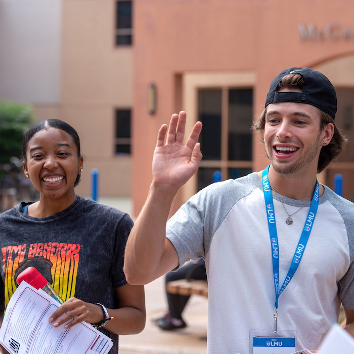 Two students smiling doing an orientation activity. The male student is wearing a hat and white shirt, the female student is wearing a Jimi Hendrix shirt.